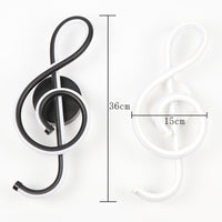 Black treble clef wall light fixture with measurements on a white background