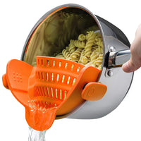 Pasta strainer with orange handle being used to drain pasta from a pot.